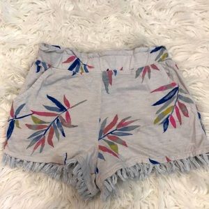 White shorts with colorful plants, fringe at the bottom, and pockets